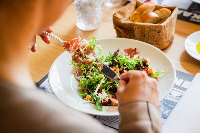 Foto de prato, com mãos indicando que alguém come uma salada.