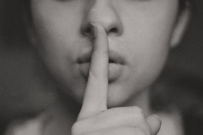 Mulher com dedo na boca apontando o gesto de silêncio