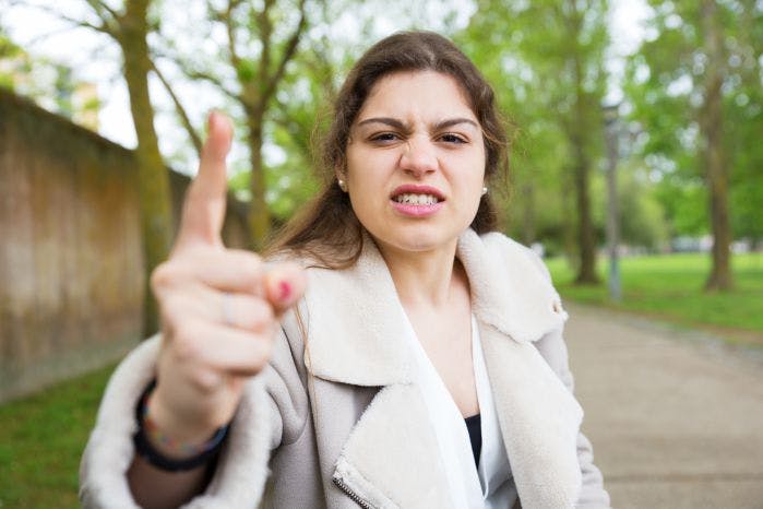 mulher com rosto bravo apontando dedo para leitor como quem reclama de algo